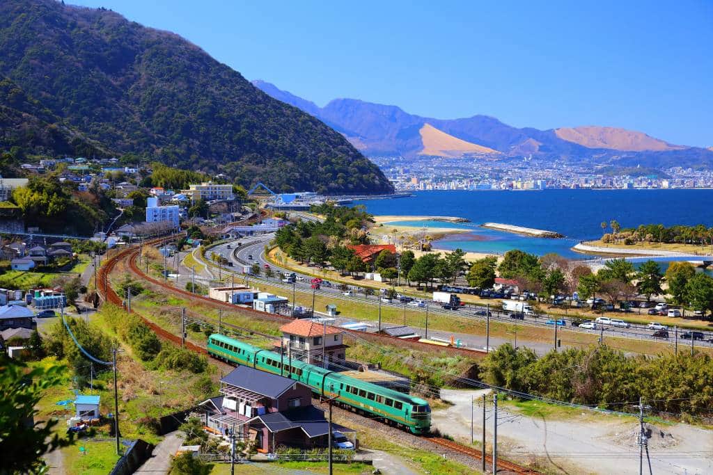 A green train travels along a curve on the coast