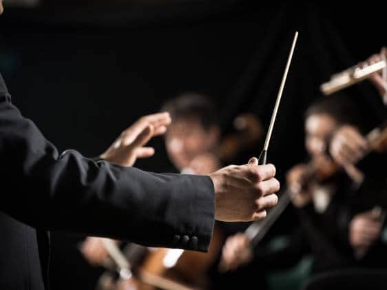 Conductor directing symphony orchestra with performers on background, hands close-up.