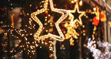 Stylish christmas golden star illumination and fir branches with red and gold baubles, golden lights bokeh on front of building at holiday market in city street. Christmas street decor