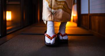Traditional Japanese ryokan house with tatami mat floor, shoji sliding paper doors and closeup of woman in kimono and geta shoes tabi socks walking in corridor
