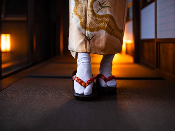 Traditional Japanese ryokan house with tatami mat floor, shoji sliding paper doors and closeup of woman in kimono and geta shoes tabi socks walking in corridor