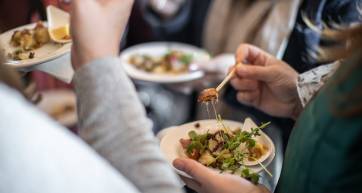 A group of people standing while they eat a tasty dish from a Fall food festival