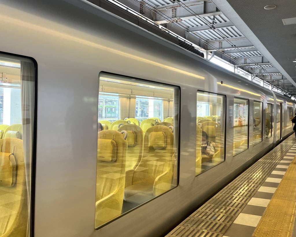 Seibu Laview limited express at the platform, yellow armchair seats visible through its oversized windows