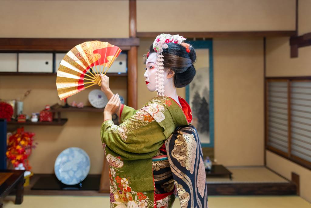 Young female tourist visiting Kyoto and experiencing Maiko (Geisha in training) makeover. Wearing traditional Japanese 'Maiko' style kimono with special white face makeup and walking around beautiful Gion district in Kyoto, Japan.
