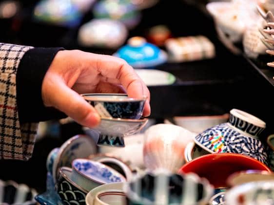 Store display closeup of ceramic pottery with tea cups teacups design and hand person picking buying in Kyoto, Japan Nishiki market street