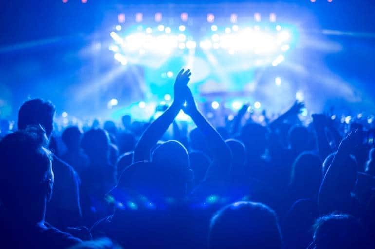 Shot of a large crowd at a music concert, enjoying a music festival event, with blue stage lights, sea of hands