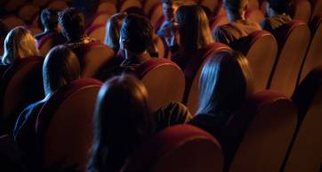 Back view of a group of young adult people sitting in the cinema and watching funny movie. They laughing and having fun.