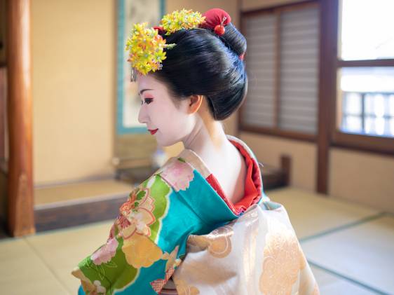 Maiko Apprentice Geisha sitting in Japanese tatami room, looking over shoulder