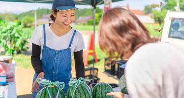 A young female farmer is selling watermelons at her farmer's market stall.